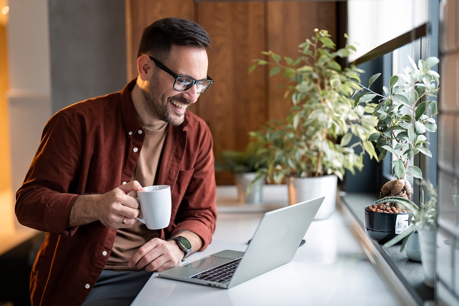 Man smiling, holding mug, using laptop.
