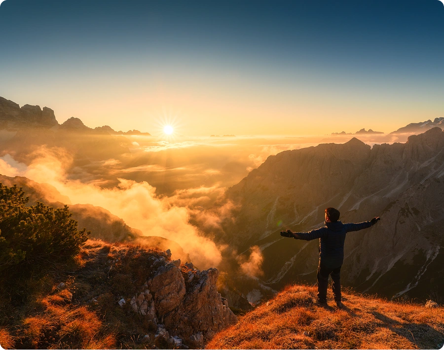 Person embracing sunrise over mountain landscape.