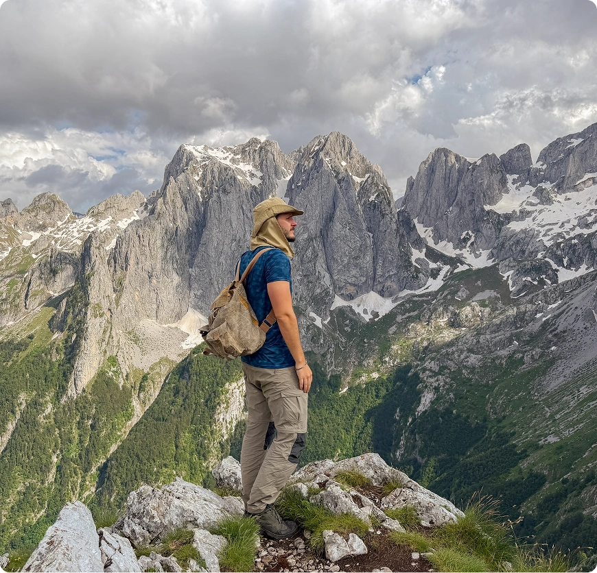 Hiker standing on rocky mountain peak, clouds.