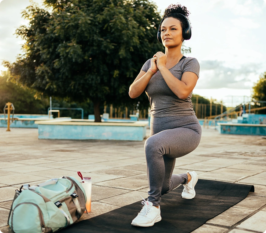 Woman exercising outdoors wearing headphones, doing lunges.