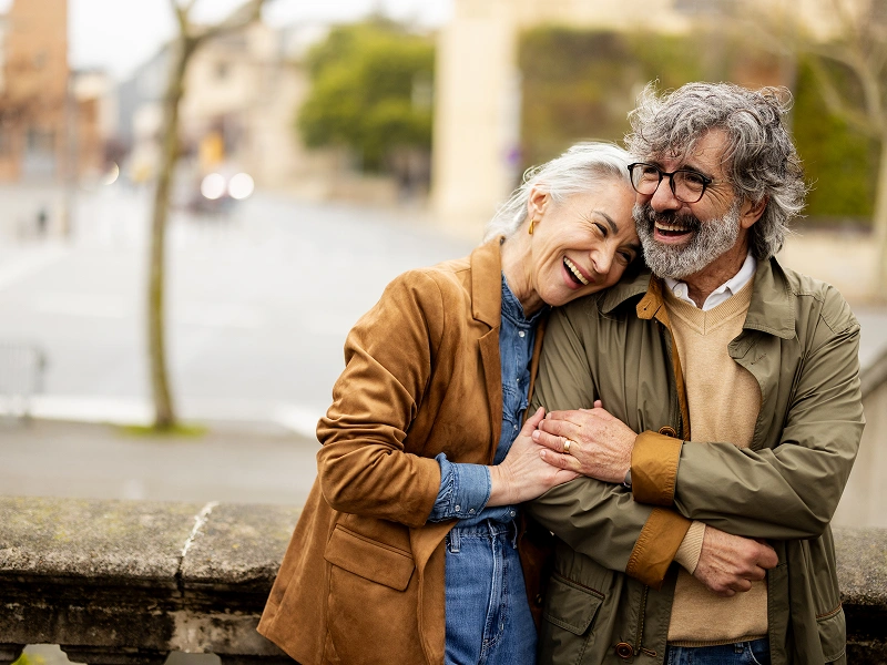 Elderly couple smiling and embracing outdoors.
