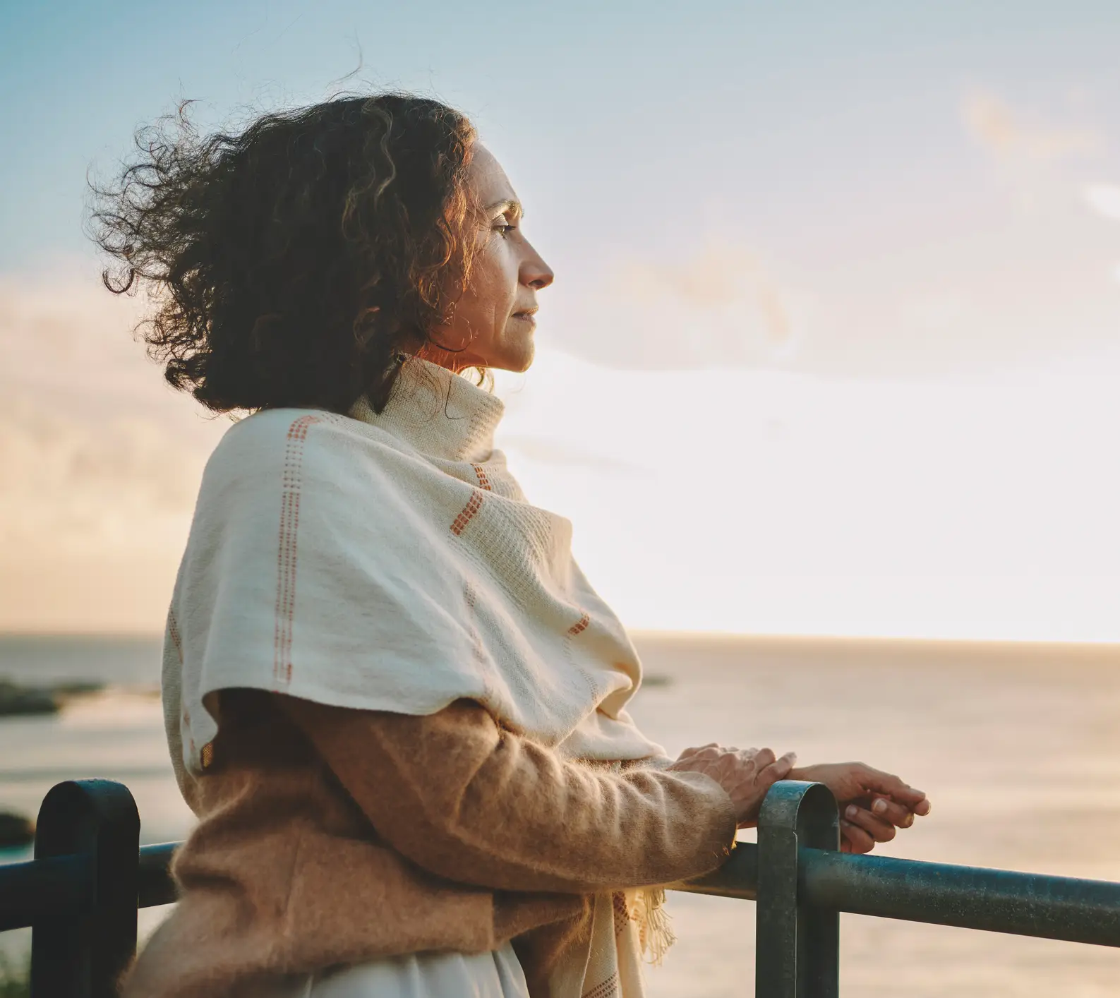 Woman in shawl gazing at ocean sunset